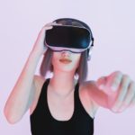 girl playing with virtual reality goggles pointing with her hand out of focus to the camera with blue and pink lights