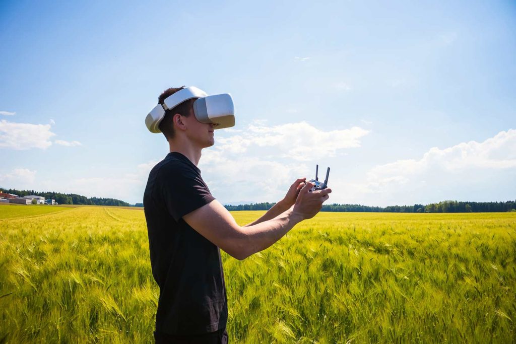 Man flying a drone with virtual reality glasses outside in nature on a wheat farming field