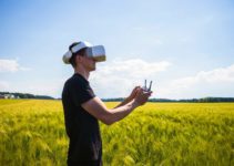 Man flying a drone with virtual reality glasses outside in nature on a wheat farming field